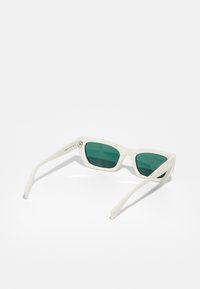 Occhiali da sole bianchi con montatura leggera, lenti verde scuro, design angolare e dettaglio del logo sul lato.