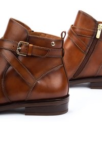 Brown leather ankle boots featuring a buckle accent, side zipper, and a low heel. Smooth texture with stitched detailing.