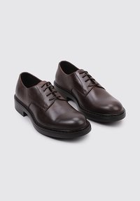 Chaussures habillées en cuir marron avec une texture lisse, bout arrondi, design à lacets et semelle noire contrastante. Style classique et minimaliste.