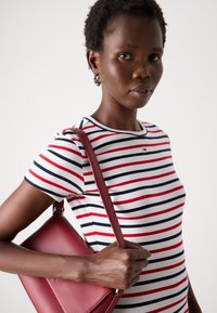 T-shirt en coton rayé en blanc, rouge et marine ; col rond ; design ajusté. Tenant un sac à main en cuir rouge profond avec une bandoulière.