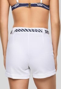 Shorts bianchi intrecciati presentano un tessuto testurizzato, un orlo arrotolato e una cintura intrecciata blu navy e bianca in vita. Vista posteriore mostrata.