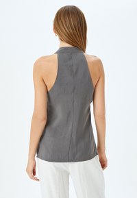 Grijze mouwloze blouse met een hoge kraag, gladde textuur en een rugnaaddetail, gecombineerd met witte, ruime broek.