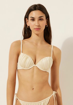 Beiger Bikini-Oberteil mit gefälteltem Design, verstellbaren dünnen Trägern und dreieckiger Form. Glatte Textur mit minimalen Hardware-Details.