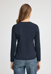 Maglietta a manica lunga di colore blu navy con scollatura rotonda, realizzata in tessuto morbido. Presenta un design aderente e dettagli di cucitura sottili, abbinata a jeans blu.