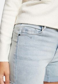 Shorts en denim bleu clair avec une finition légèrement usée, design à cinq poches et taille ajustée, complétée par un doux pull blanc.