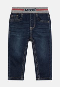 Jean en denim bleu foncé avec une taille élastique grise ornée de lettres rouges. Comprend des poches avant et des détails de couture jaunes.