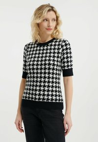 Svetr z pletené látky se vzorem houndstooth v černobílém provedení, s krátkými rukávy, kulatým výstřihem a černým žebrovaným lemem a manžetami.