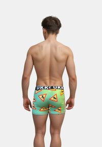 Boxer in verde con un motivo ripetuto di triangoli di avvertimento e figure nere, vita adornata da un elastico nero con marchio.