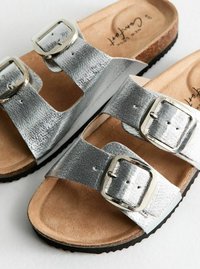 Sandalias metálicas plateadas con dos correas ajustables que presentan herrajes de hebilla cuadrada, plantilla acolchada en tono marrón y suela negra duradera.