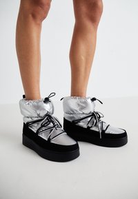 Silver and black sneakers with a padded top, featuring lace detailing and a rubber sole. The upper is shiny, and the design is chunky.