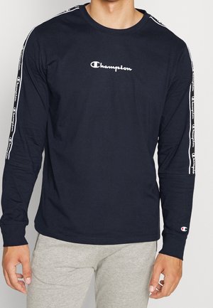 T-shirt à manches longues en coton de couleur marine, avec un logo Champion blanc sur la poitrine et des rayures logo le long des manches.