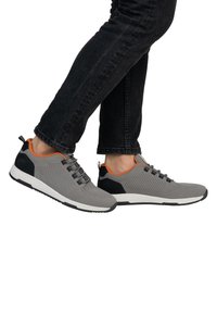 Graue Netzsneaker mit schwarzem Rückenteil und orangefarbenen Akzenten. Sie verfügen über ein strukturiertes Design und eine Schnürung, vor einem schlichten Hintergrund.