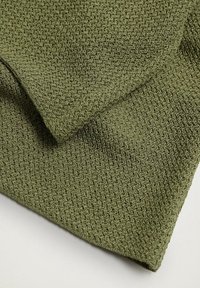 Tissu vert olive plié avec un motif tricoté texturé en boucle, présenté sur un fond pâle.