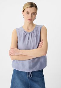 Jasnoniebieski bezrękawnik z marszczonym dekoltem, miękką teksturą i luźnym krojem, w zestawieniu ze spódnicą dżinsową.