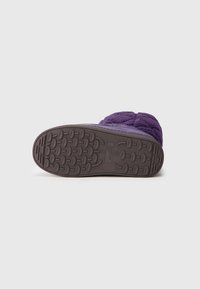 Zapatilla púrpura con parte superior texturizada y suela de goma que presenta un diseño circular para un mejor agarre. Diseño acogedor con un acabado suave.