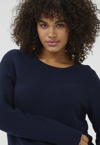 Navy ribbed sweater with a crew neckline and long sleeves, featuring a textured fabric and fitted design.