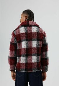 Rood-grijs geruit bontjack met een zachte, gestructureerde afwerking, voorzien van een brede kraag en een ontspannen pasvorm. Geen zichtbare sluitingen.