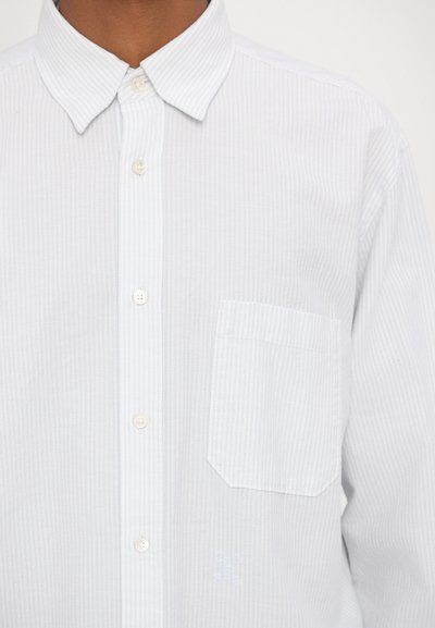 Camisa blanca de botón con rayas azul claro, un cuello clásico, un bolsillo en el pecho y un sutil bordado en la textura de la tela.