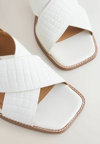 Sandales en cuir blanc avec larges brides croisées texturées et semelles cousues marron, avec un design à bout carré.