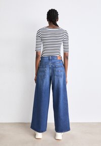 Breda blåjeans med ljus tvätt, parat med en svart- och vitrandig långärmad topp. Har två bakfickor och en läderpatch.