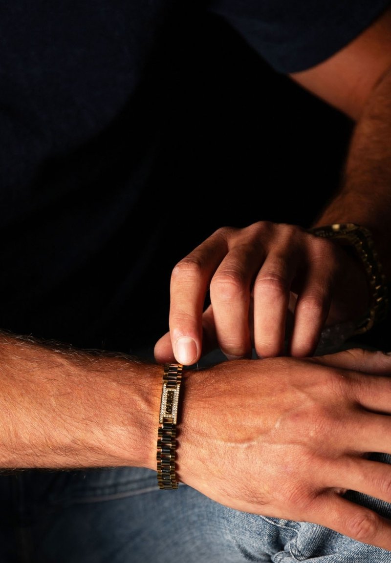 Bracciale in oro con chiusura rettangolare, maglie testurizzate e accenti di pietre simili a cristalli. Mano che regola il bracciale su un polso.