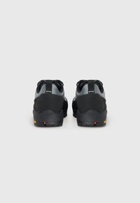 Black and gray footwear with a textured upper, reinforced heel, and a rugged sole featuring a bright red accent. Two pull tabs at the back.