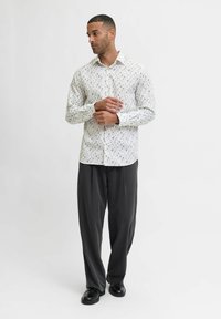 Valkoinen nappipaita, jossa on kukkakuosi, yhdistettynä harmaisiin housuihin ja mustiin kenkiin. Paidassa on normaali kaulus ja pitkät hihat.