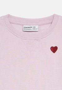 Jasnoróżowa bluza z prążkowanym, okrągłym dekoltem, z małym czerwonym błyszczącym serduszkiem na lewej stronie klatki piersiowej.