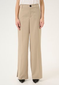 Pantalon ample taille haute beige en tissu lisse, avec une fermeture à bouton, des plis marqués et des fentes sur l'ourlet.