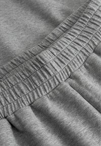 A szürke pamut anyag gyűrt elasztikus derekát mutatja be, texturált részletekkel és sima varrásokkal, amelyek jól illeszkednek a puha anyaghoz.