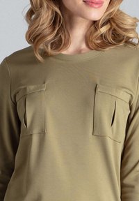 Oliwkowy, długi rękaw, górna część wykonana z gładkiego materiału, z dwoma kieszeniami na piersi z klapkami, okrągły dekolt i luźny krój.