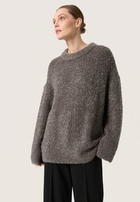 Oversized grå sweatshirt lavet af et tekstureret, fluffy stof, med bred halsudskæring og løstsiddende ærmer, parret med sorte bukser.