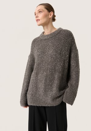 Oversized gray sweater with a textured, fuzzy fabric, wide neckline, and loose-fitting sleeves, paired with black trousers.