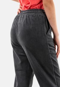 Pantalones de pana en gris oscuro con textura acanalada, cinturilla elástica y bolsillos laterales. El diseño presenta un ajuste holgado y un brillo sutil.
