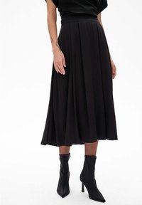 Zwarte plooien midi-rok gemaakt van glad stof, met een hoge tailleband en een vloeiende silhouet, gecombineerd met slanke zwarte enkellaarsjes.
