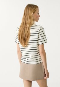 Gestreepte kortek mouw top in wit en zwart, met een ronde hals en een casual pasvorm, gecombineerd met een lichtbeige rok.