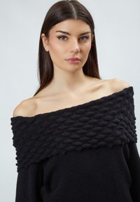 Schwarzer schulterfreier Pullover mit einem strukturierten, erhabenen Muster am Ausschnitt und einem glatten, gestrickten Körper.