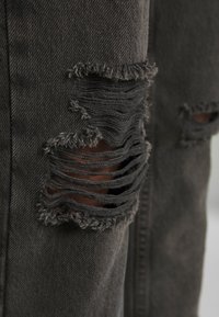 Grå denim med fransiga revor och slitna detaljer som visar en texturerad, sliten look. Har en rak passform med subtila hårdvarudetaljer.