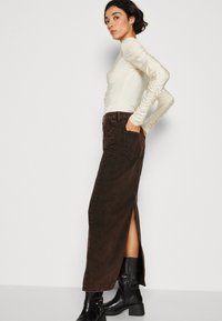 Cremefarvet langærmet top med samlet detalje på ærmerne, parret med en højtaljet, mørkebrune denim maxi-nederdel med sideslids og lommer.