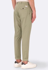 Chinos verde oliva chiaro con fitting dritto, orli arrotolati, tasche laterali e tasche posteriori doppie con chiusure a bottone. Abbinati a sneakers bianche.