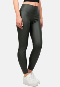 Leggings a vita alta di colore verde oliva, realizzati in materiale elasticizzato e lucido. Texture liscia senza cuciture visibili, abbinati a sneakers bianche.