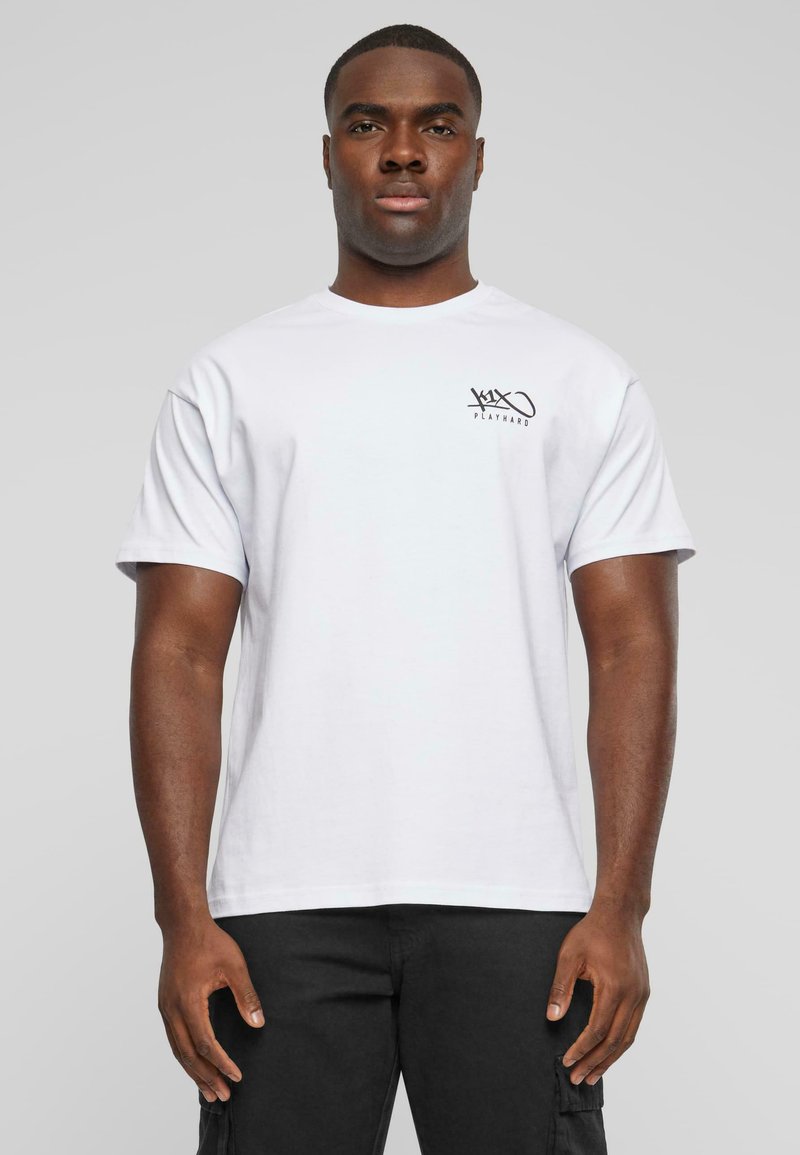 White cotton t-shirt with short sleeves, featuring a small black graphic on the left chest. Model wearing black cargo pants, standing upright.