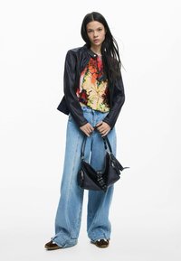 Fekete bőrdzseki; színes mintás felső; túlméretezett kék farmernadrág; fekete táska ezüst fém alkatrészekkel; barna mintás cipő.