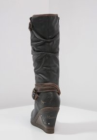Stivale alto in pelle nera con design slouchato, dettaglio con cinturino marrone, finitura testurizzata e tacco a zeppa con logo laterale.