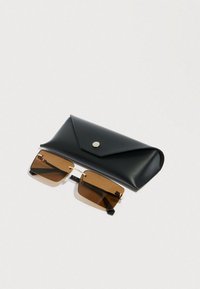 Occhiali da sole rettangolari con lenti marroni e montatura sottile in metallo accanto a una custodia nera in pelle chiusa con un bottone a pressione su sfondo bianco.