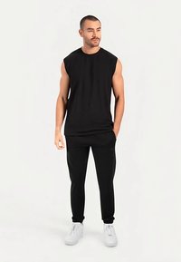 Black sleeveless shirt paired with black tapered pants and white sneakers, featuring a simple, minimalist design and smooth fabric texture.