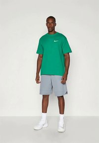 Green cotton t-shirt with a small white Nike logo, paired with grey shorts. Model wearing white sneakers and white crew socks.