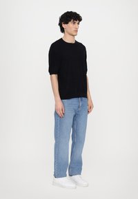 Črna kratka majica s sproščenim krojem, v kombinaciji s svetloblue jeans hlačami ravnega kroja in belimi športnimi copati. Preprost, sproščen outfit.