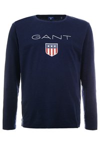 Marineblaues Langarmhemd aus Baumwolle mit einem weißen "GANT"-Logo und einem Schilddesign mit roten und blauen Streifen auf der Vorderseite.