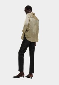Camicia a righe oversize gialla e nera, abbinata a pantaloni neri a sigaretta e scarpe con tacco a cono nere.